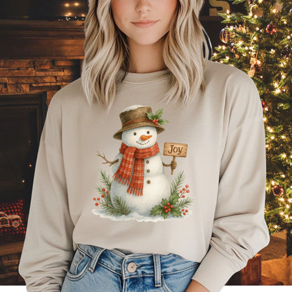 Beige long-sleeve cotton tee with a watercolor snowman holding a "Joy" sign, holly, and snowy branches.
