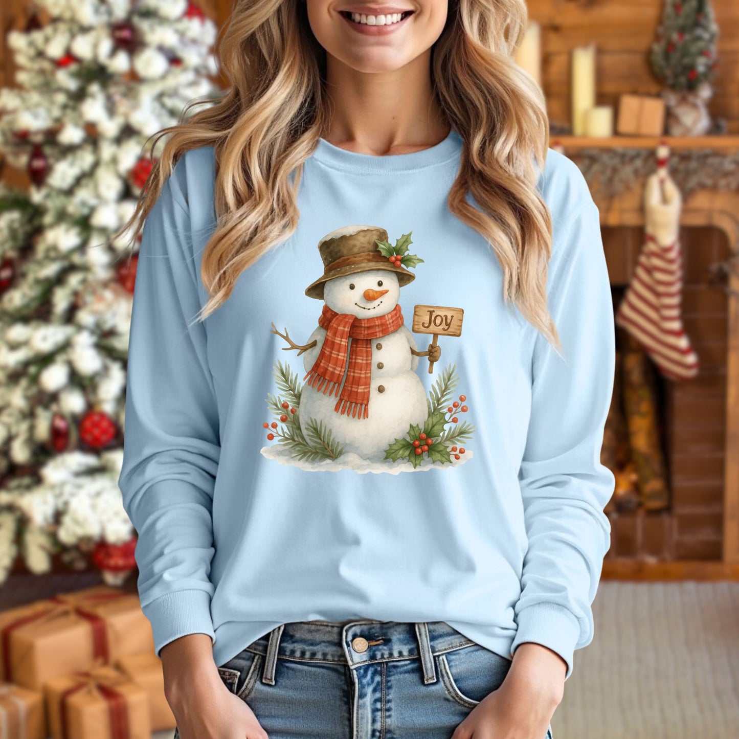 Light blue long-sleeve cotton tee with a watercolor snowman holding a "Joy" sign, holly, and snowy branches.