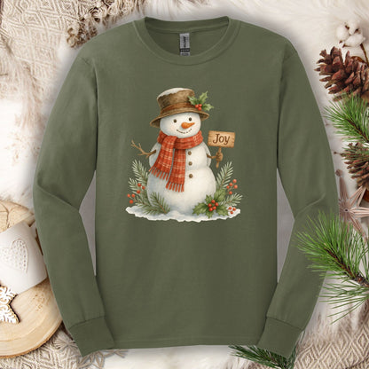 Military Green long sleeve tee with a watercolor snowman holding a "Joy" sign, holly, and snowy branches.