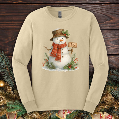 Sand long sleeve tee with a watercolor snowman holding a "Joy" sign, holly, and snowy branches.