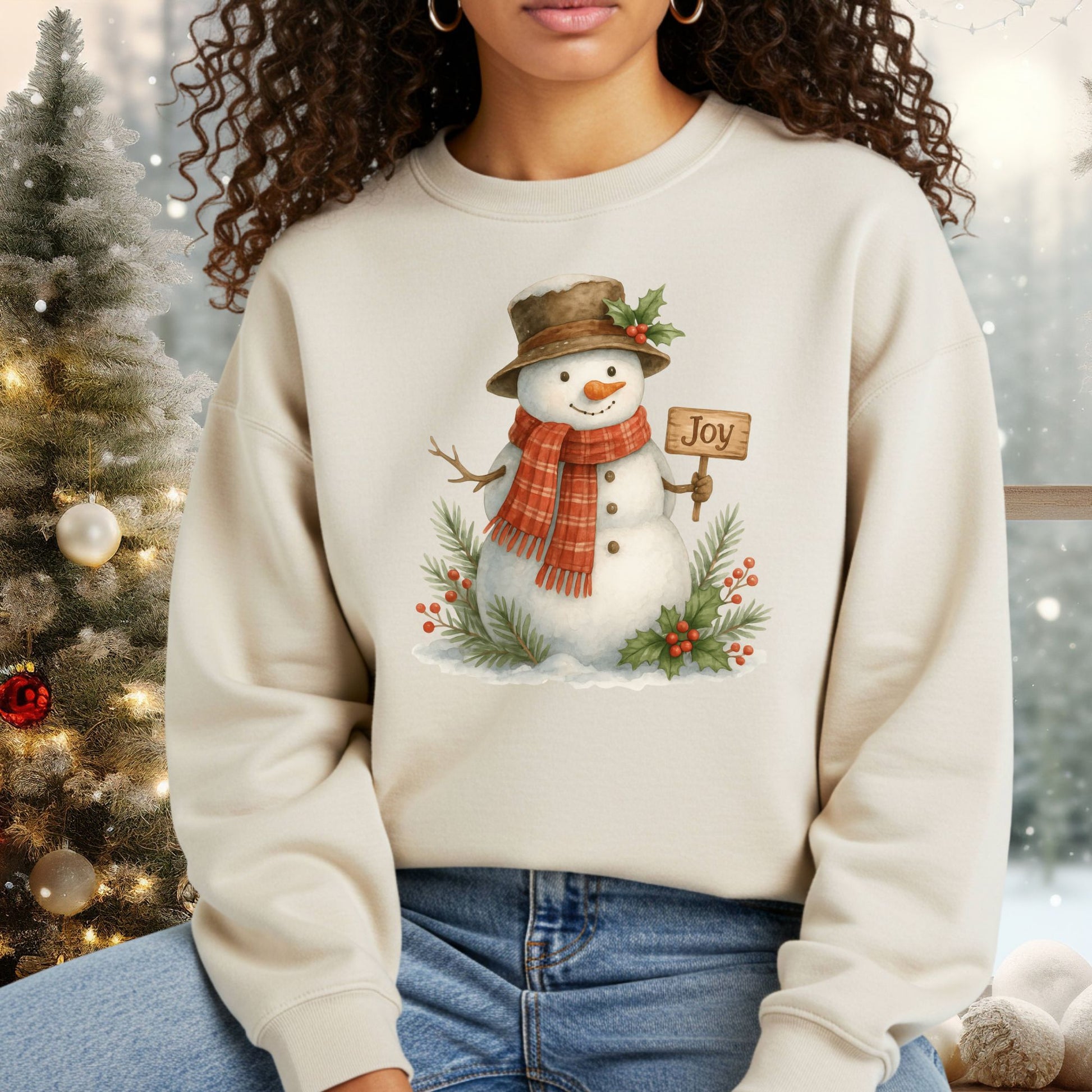 Beige Gildan 18000 sweatshirt with a watercolor snowman holding a "Joy" sign, holly, and snowy branches.