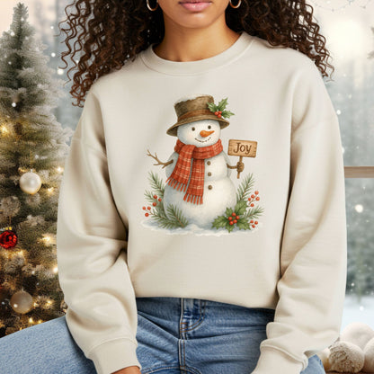 Beige Gildan 18000 sweatshirt with a watercolor snowman holding a "Joy" sign, holly, and snowy branches.