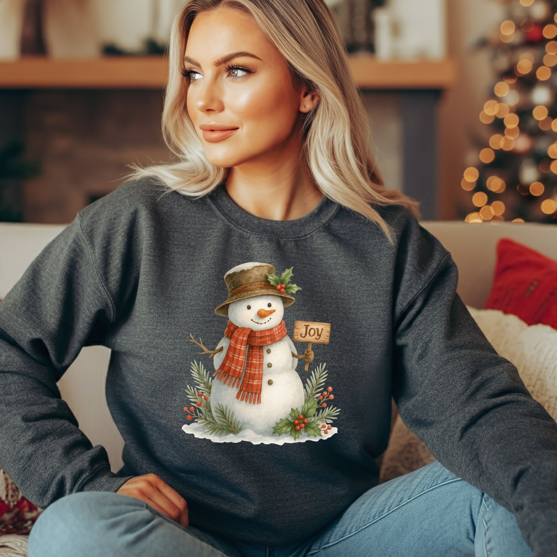 Woman wearing a charcoal gray sweatshirt with a watercolor snowman holding a "Joy" sign.