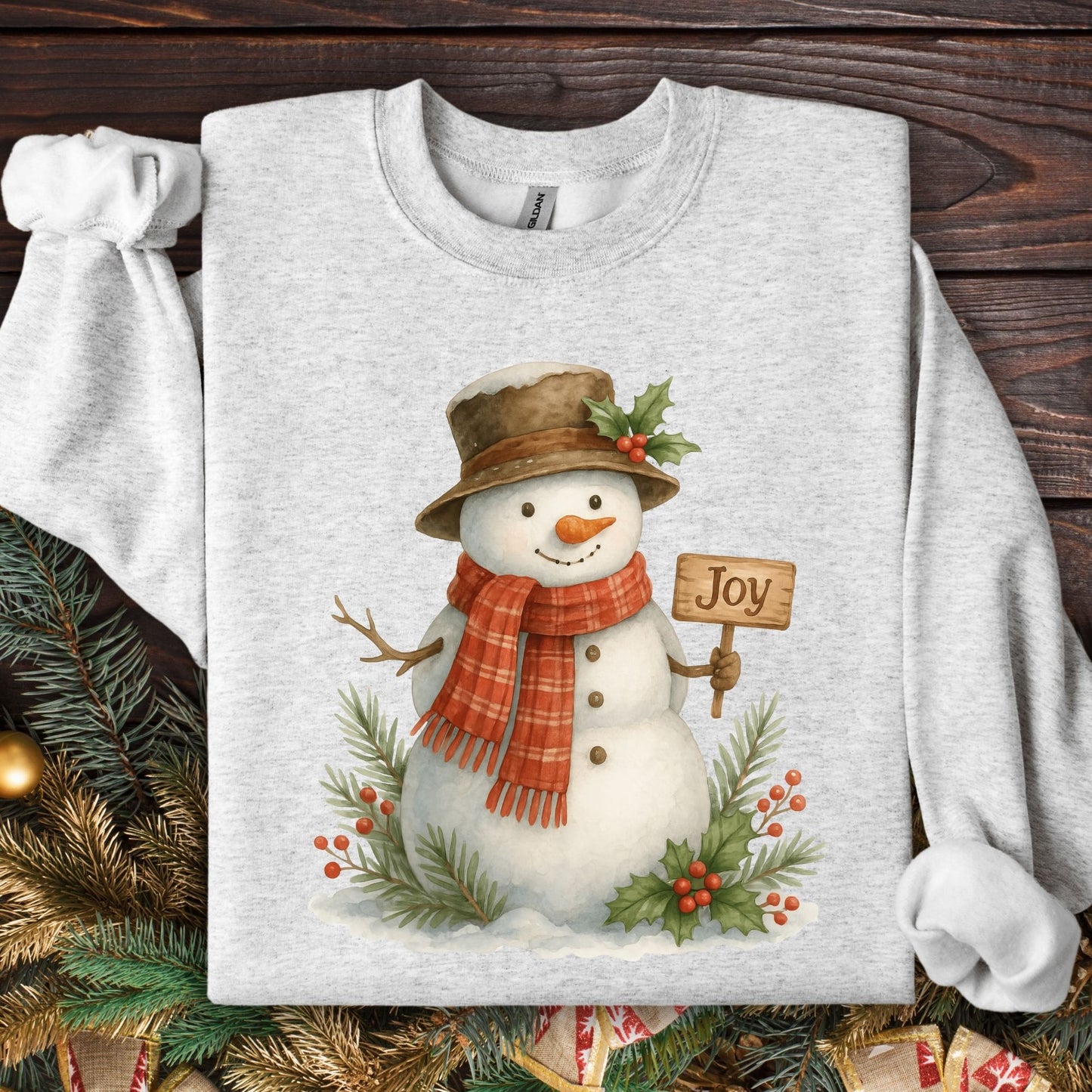 Ash Gildan 18000 sweatshirt with a watercolor snowman holding a "Joy" sign, surrounded by holly and snowy branches.
