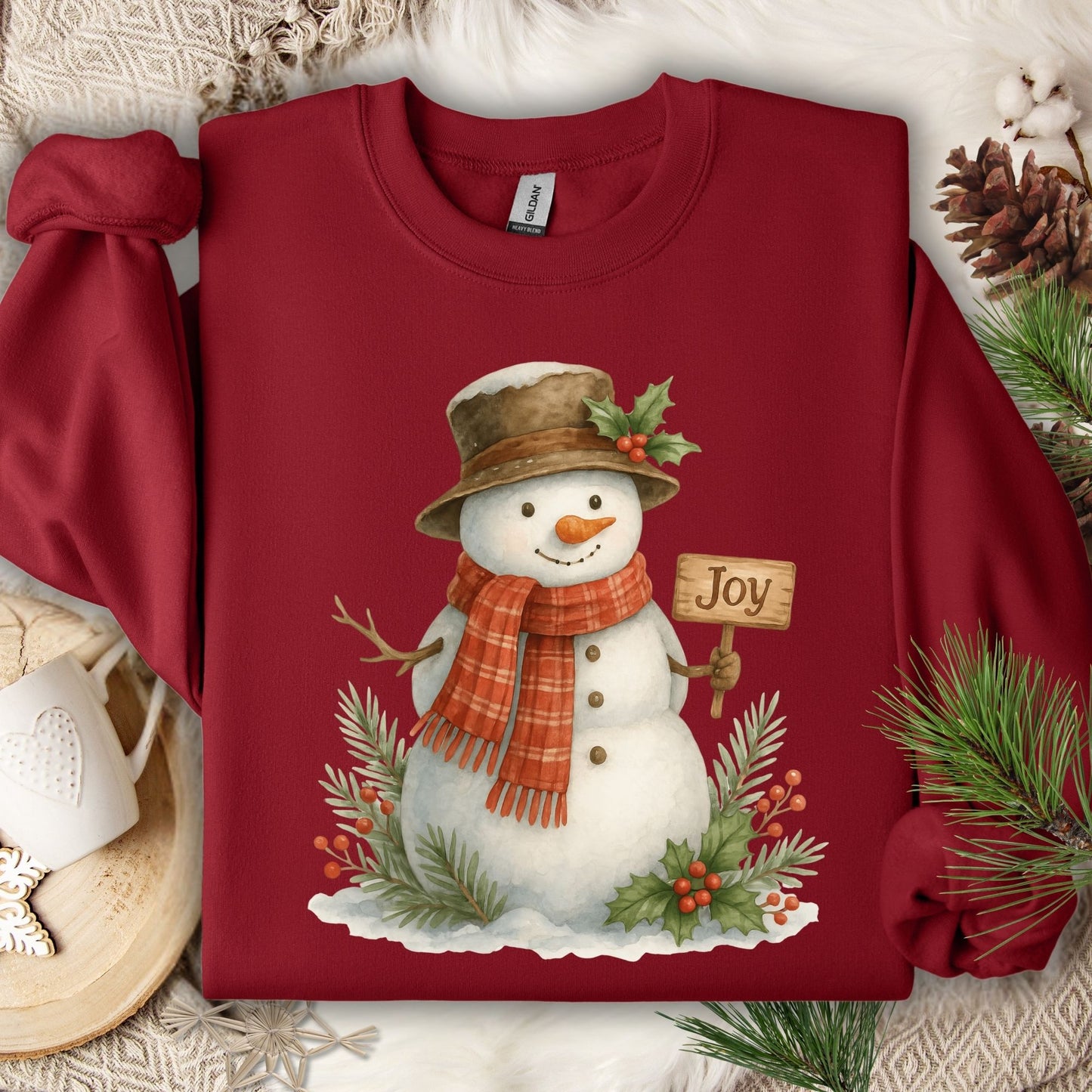 Cardinal Red Gildan 18000 sweatshirt with a watercolor snowman holding a "Joy" sign, holly, and snowy branches.