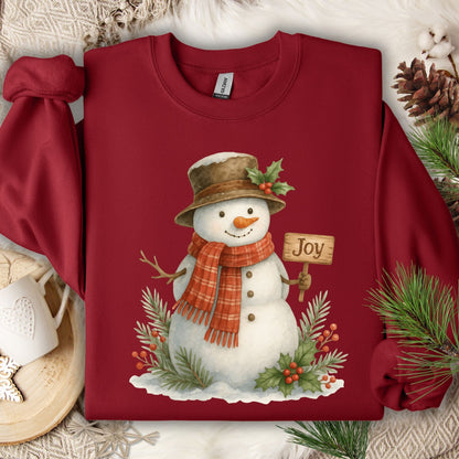 Cardinal Red Gildan 18000 sweatshirt with a watercolor snowman holding a "Joy" sign, holly, and snowy branches.