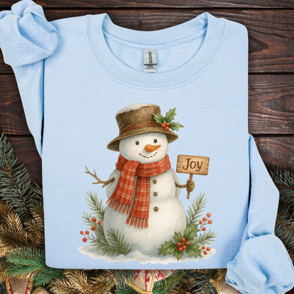Light blue Gildan 18000 sweatshirt with a watercolor snowman holding a "Joy" sign, holly, and snowy branches.