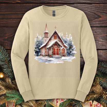 Sand long sleeve tee with a rustic, snow-dusted wooden chapel, evergreens, holly, and pine garland.