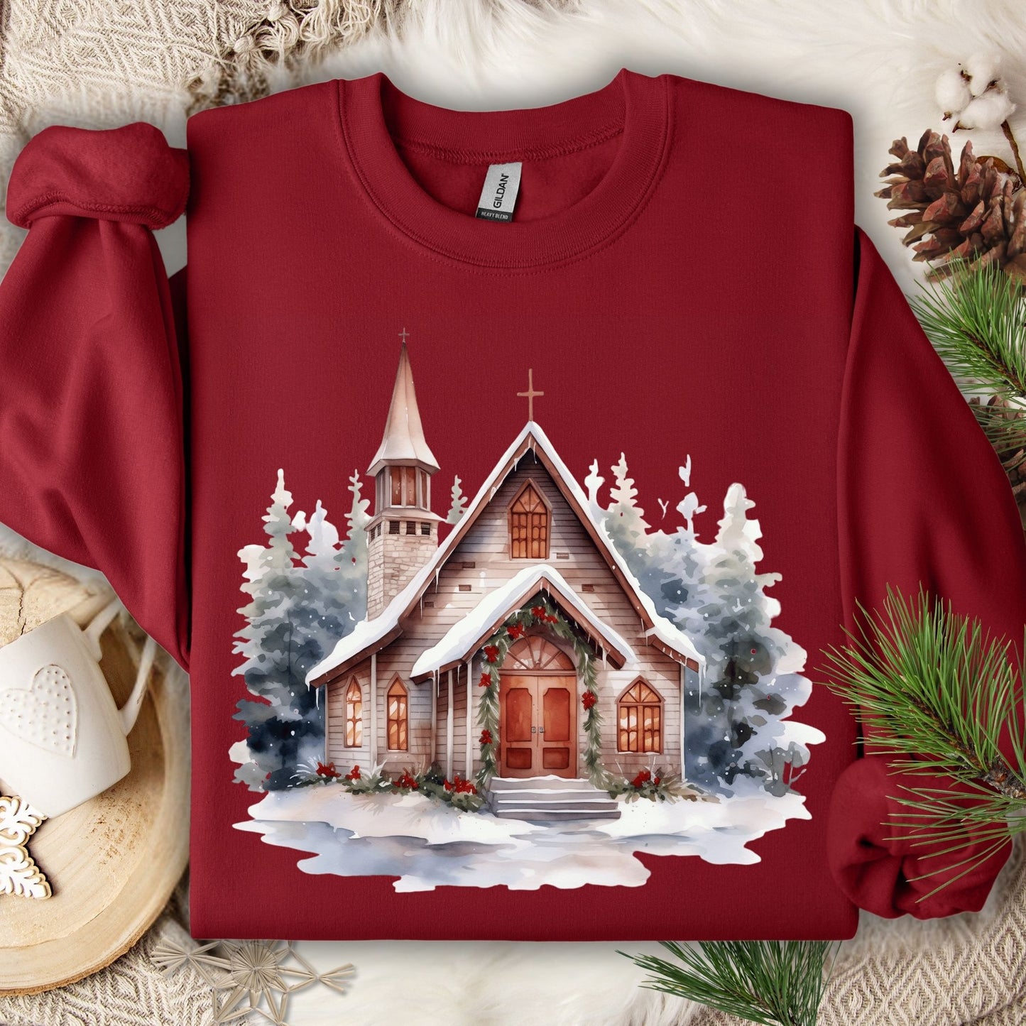 Cardinal Red Gildan sweatshirt with a watercolor rustic chapel in snow, festive greenery, and evergreens.