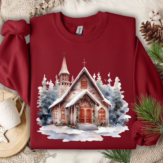 Cardinal Red Gildan sweatshirt with a watercolor rustic chapel in snow, festive greenery, and evergreens.