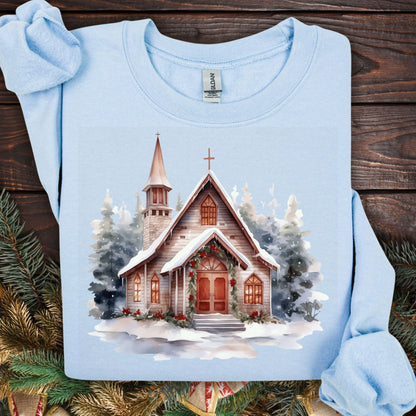 Light blue Gildan sweatshirt, size S, with a watercolor rustic chapel in snow and Christmas greenery.