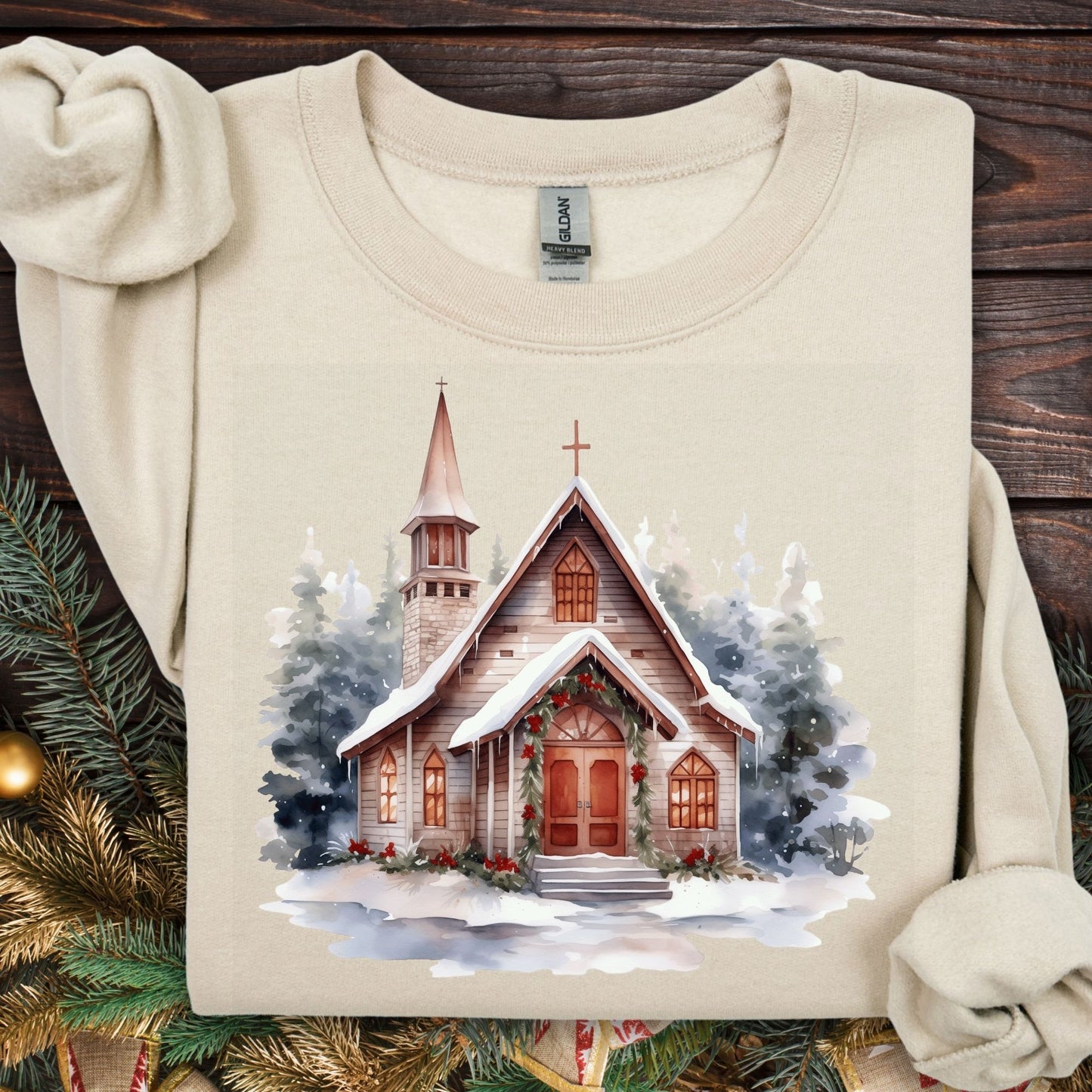 Sand Gildan sweatshirt with watercolor rustic chapel in snow, festive greenery.
