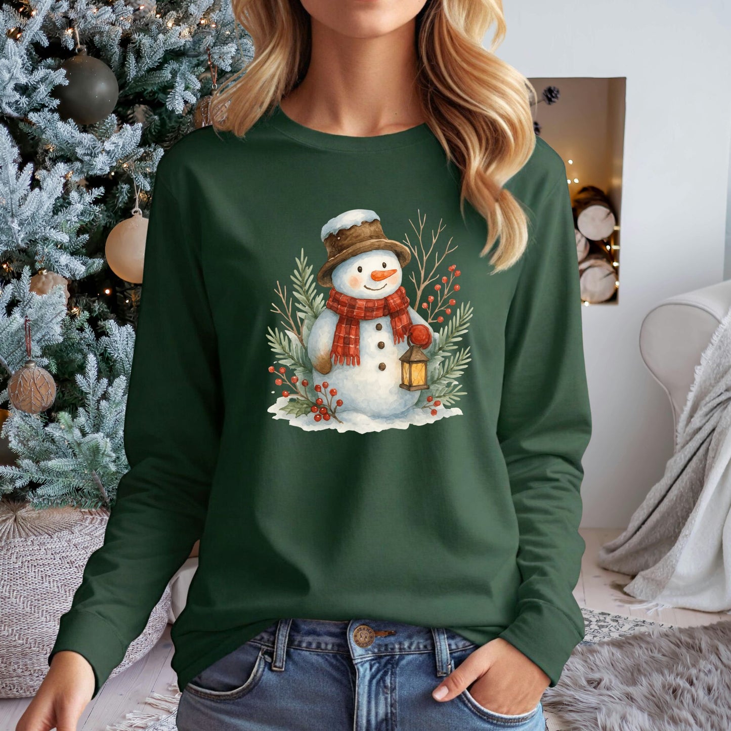 Green long-sleeve tee with a watercolor snowman holding a lantern, surrounded by snowy branches.