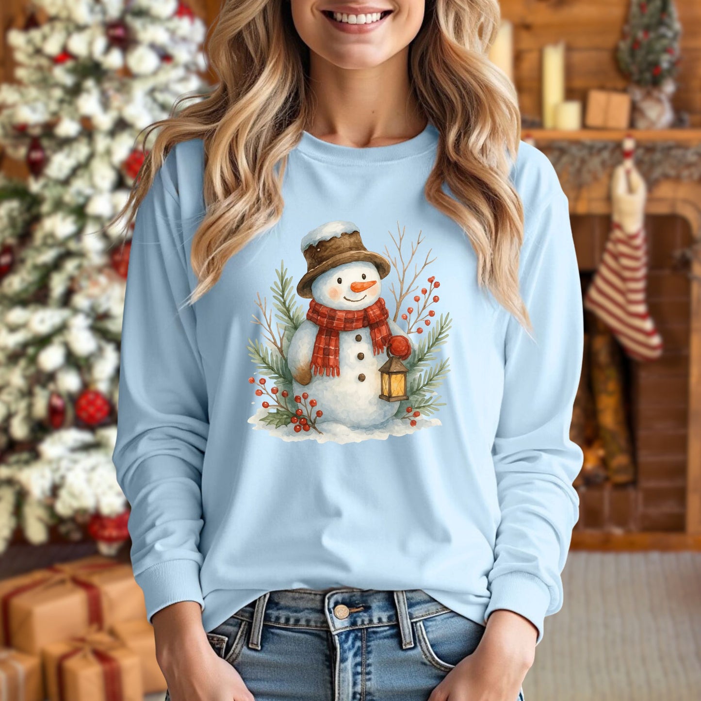 Light blue long-sleeve tee with a watercolor snowman holding a lantern, worn by a woman.
