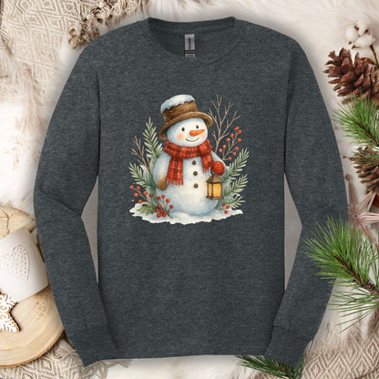 Dark Heather long sleeve tee with a watercolor snowman holding a lantern, surrounded by snowy branches.