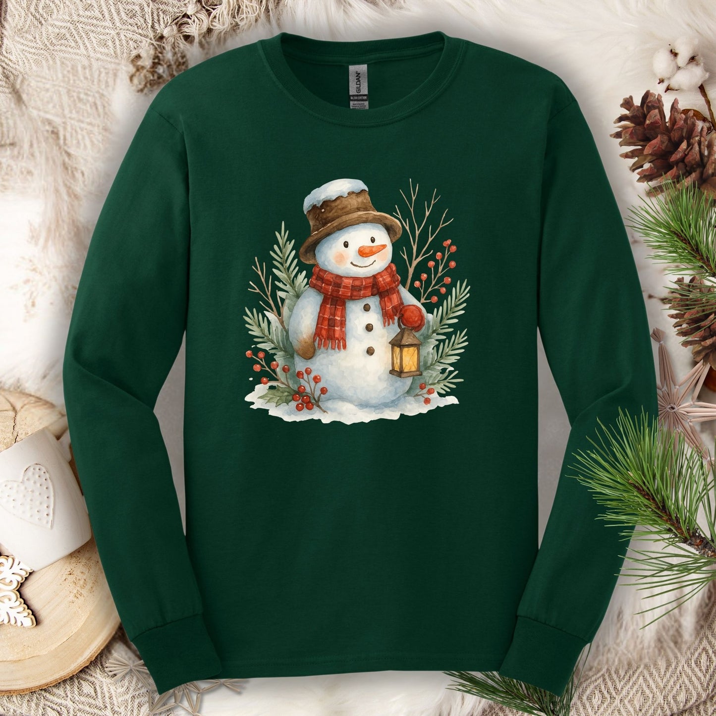 Forest Green long sleeve tee with a watercolor snowman holding a lantern, surrounded by snowy branches.