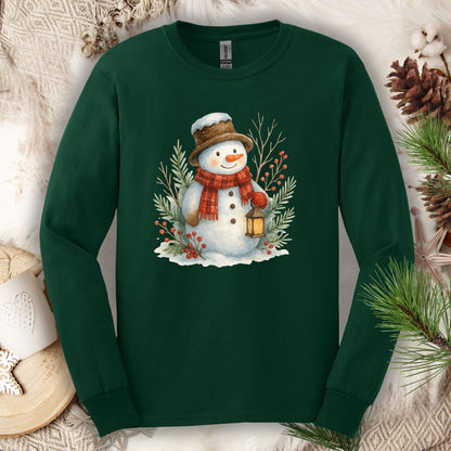 Forest Green long sleeve tee with a watercolor snowman holding a lantern, surrounded by snowy branches.