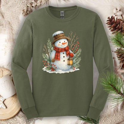 Military Green long sleeve tee with a watercolor snowman holding a lantern, surrounded by snowy branches.