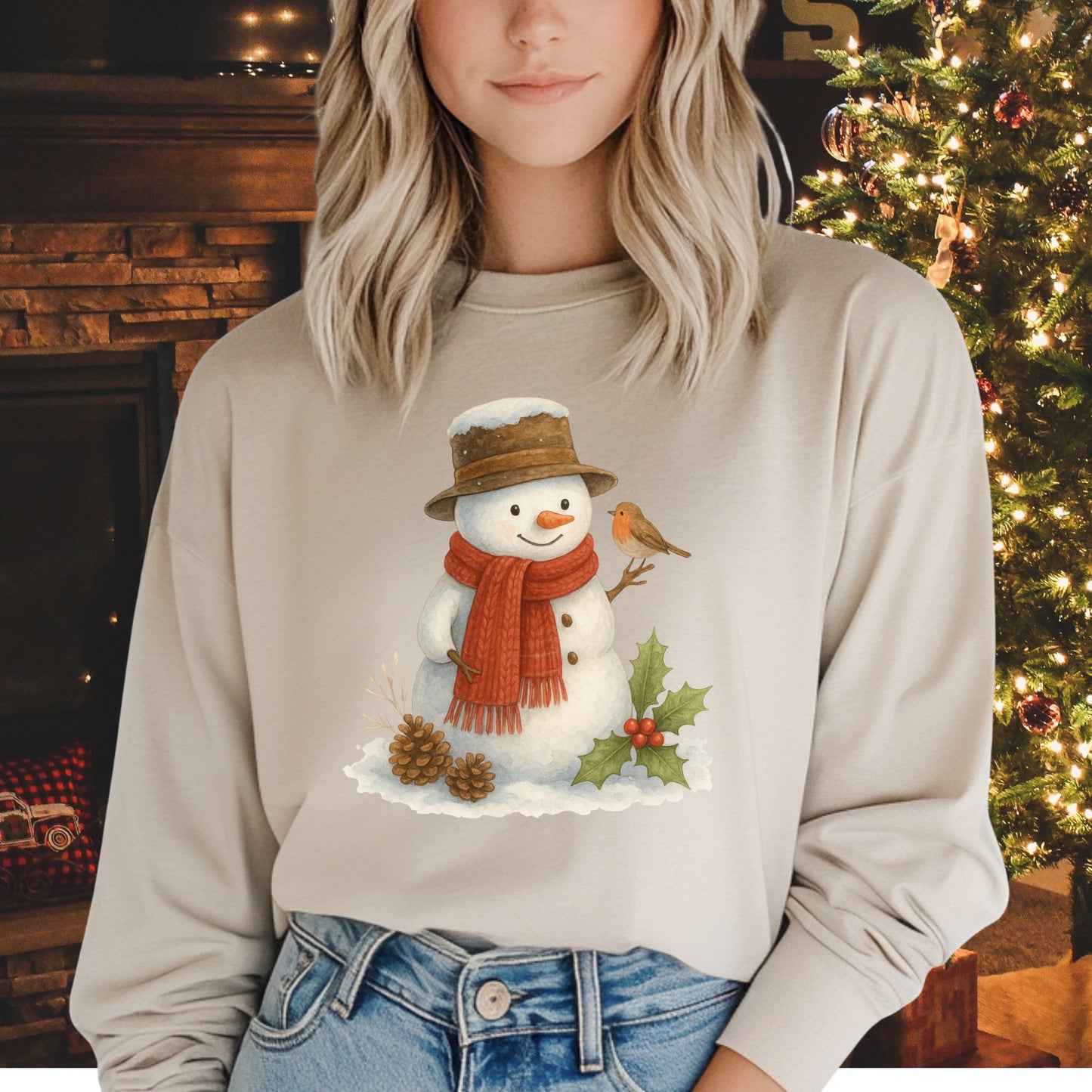 Beige long-sleeve tee with a rustic watercolor snowman, holly, pinecones, and a sparrow.
