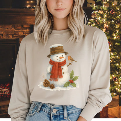 Beige long-sleeve tee with a rustic watercolor snowman, holly, pinecones, and a sparrow.
