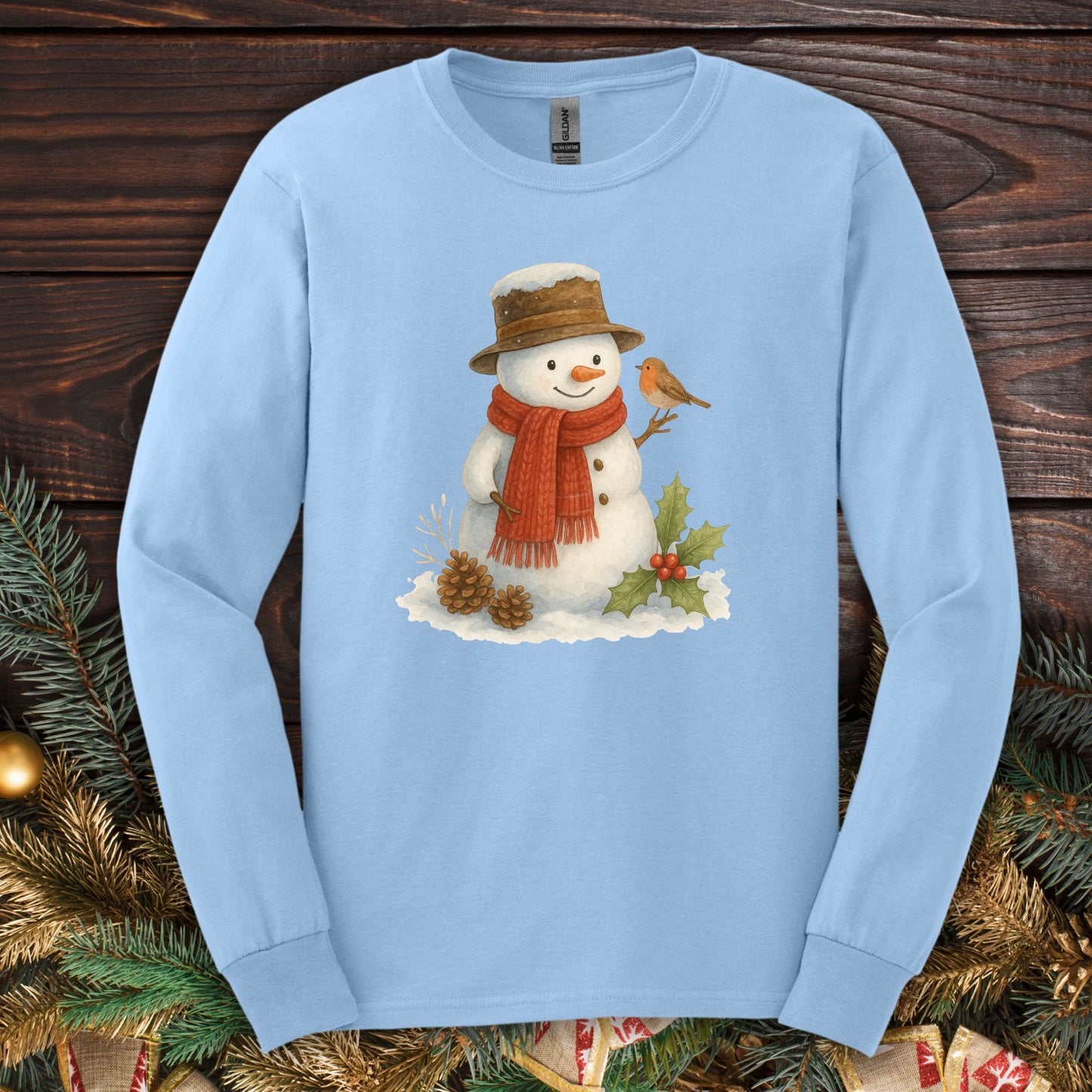 Light blue long sleeve tee with a rustic watercolor snowman, sparrow, holly, and pinecones.
