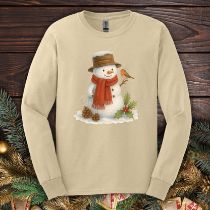 Sand Gildan long sleeve tee with a rustic watercolor snowman holding a sparrow, holly, and pinecones.