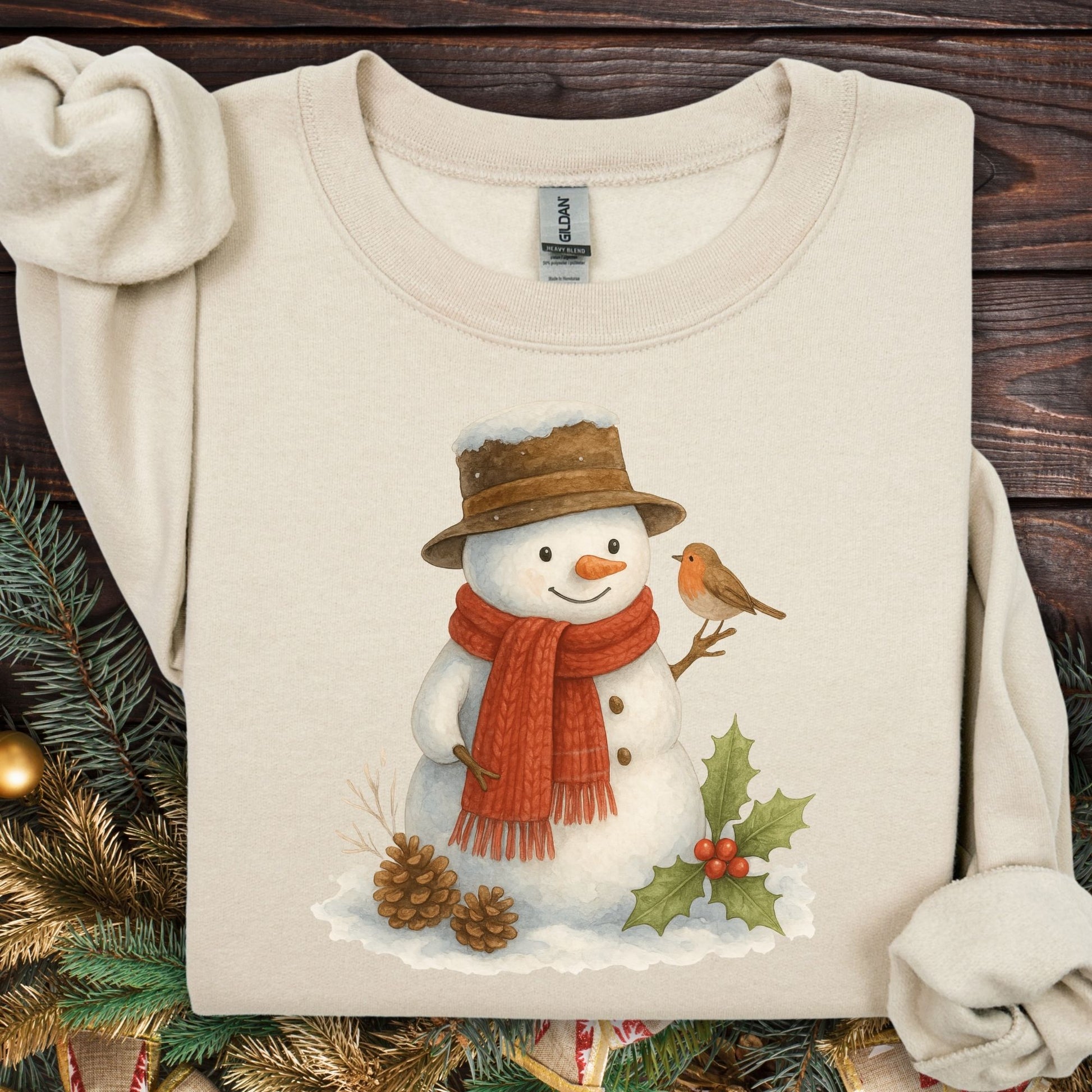 Beige Gildan 18000 sweatshirt with a watercolor snowman, brown hat, red scarf, sparrow, holly, and pinecones.