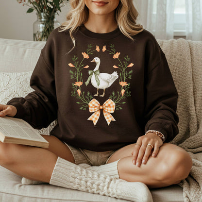 Woman in a dark brown crewneck sweatshirt with a goose, wildflower, and butterfly wreath design.