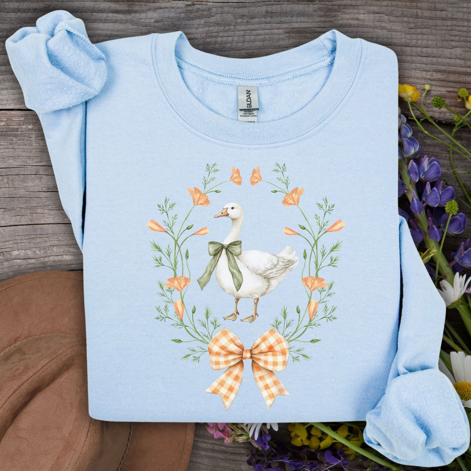 Light blue crewneck sweatshirt with a farmhouse goose, green ribbon, wildflowers, and orange gingham bow design.