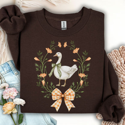 Dark chocolate crewneck sweatshirt with a white goose in a floral wreath, tied with a green ribbon and orange gingham bow.