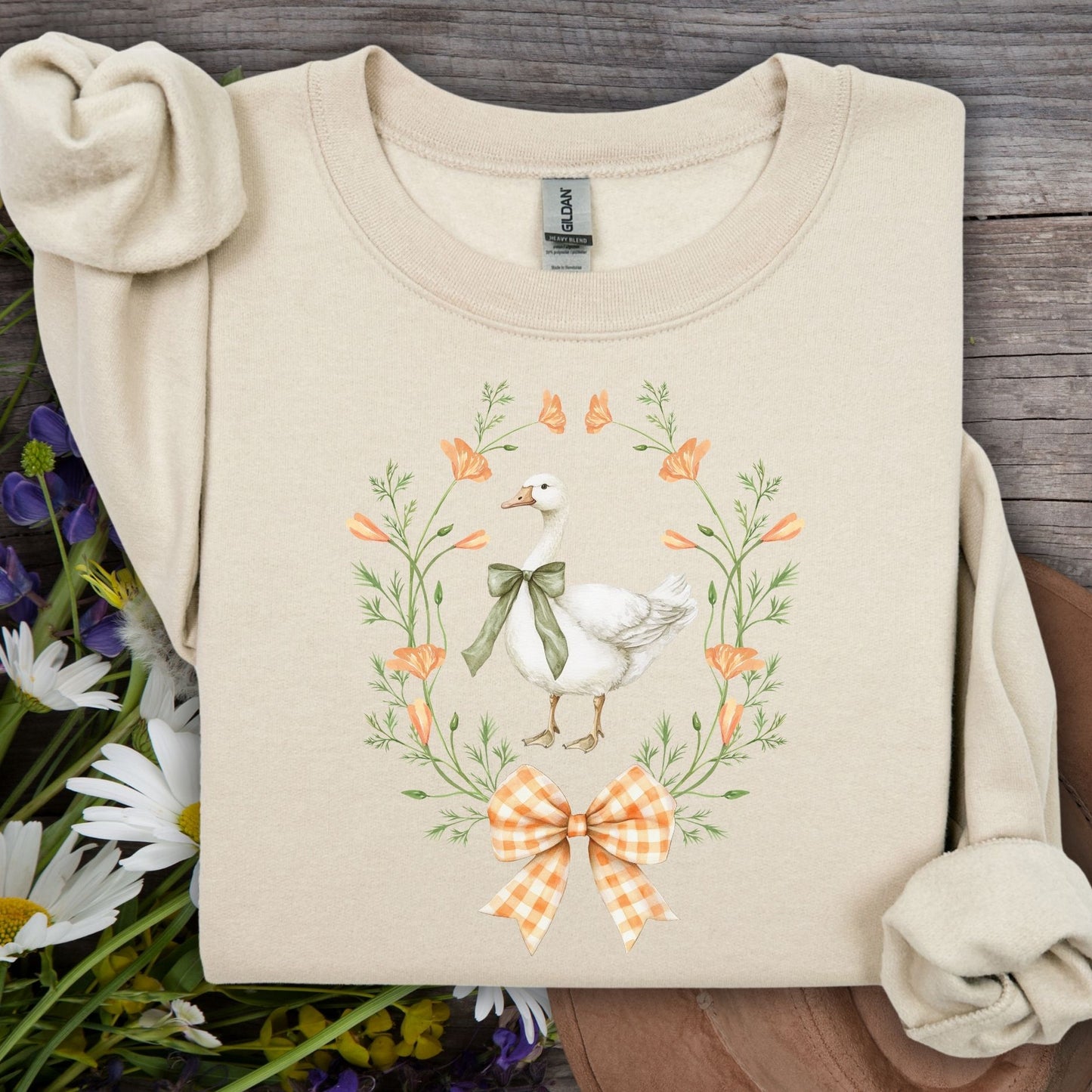 Sand colored crewneck sweatshirt with a goose in a floral wreath and gingham bow design.