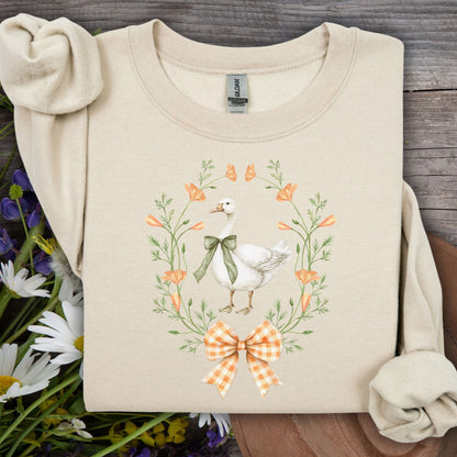 Sand colored crewneck sweatshirt with a goose in a floral wreath and gingham bow design.