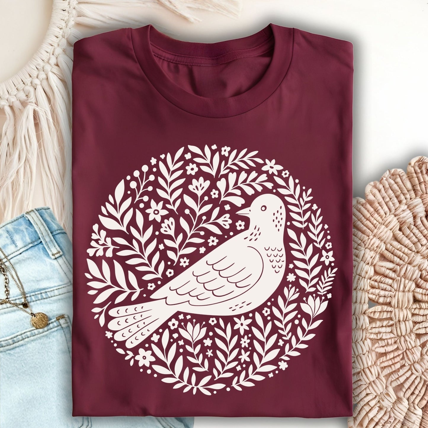 Maroon S-sized t-shirt with a white Scandinavian bird and floral wreath design.