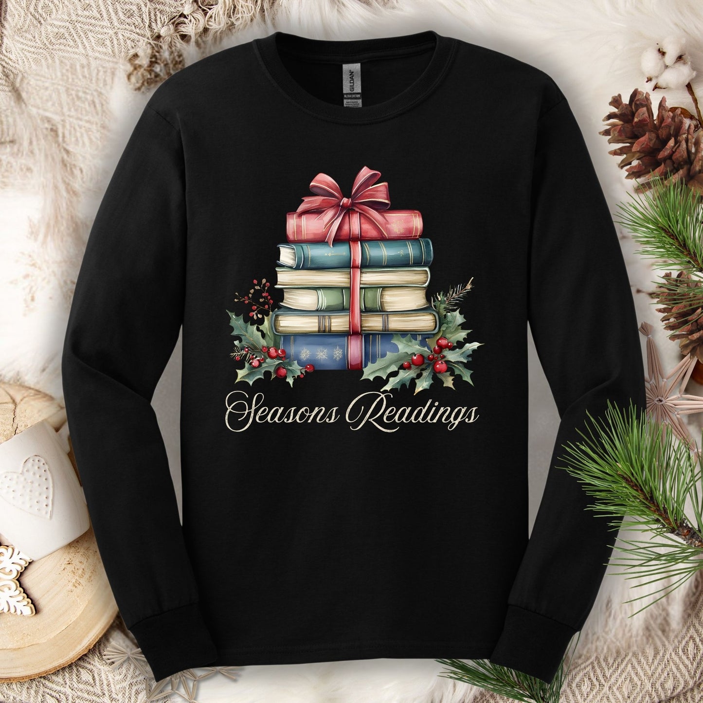 Black long sleeve tee with watercolor stack of vintage Christmas books, a pink bow, holly, and "Seasons Readings" text.