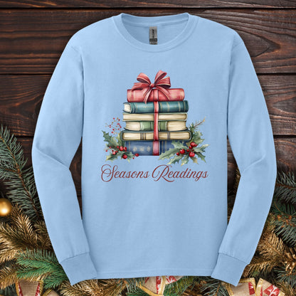 Light blue long sleeve tee with watercolor stacked Christmas books, red bow, holly, and "Seasons Readings" text.