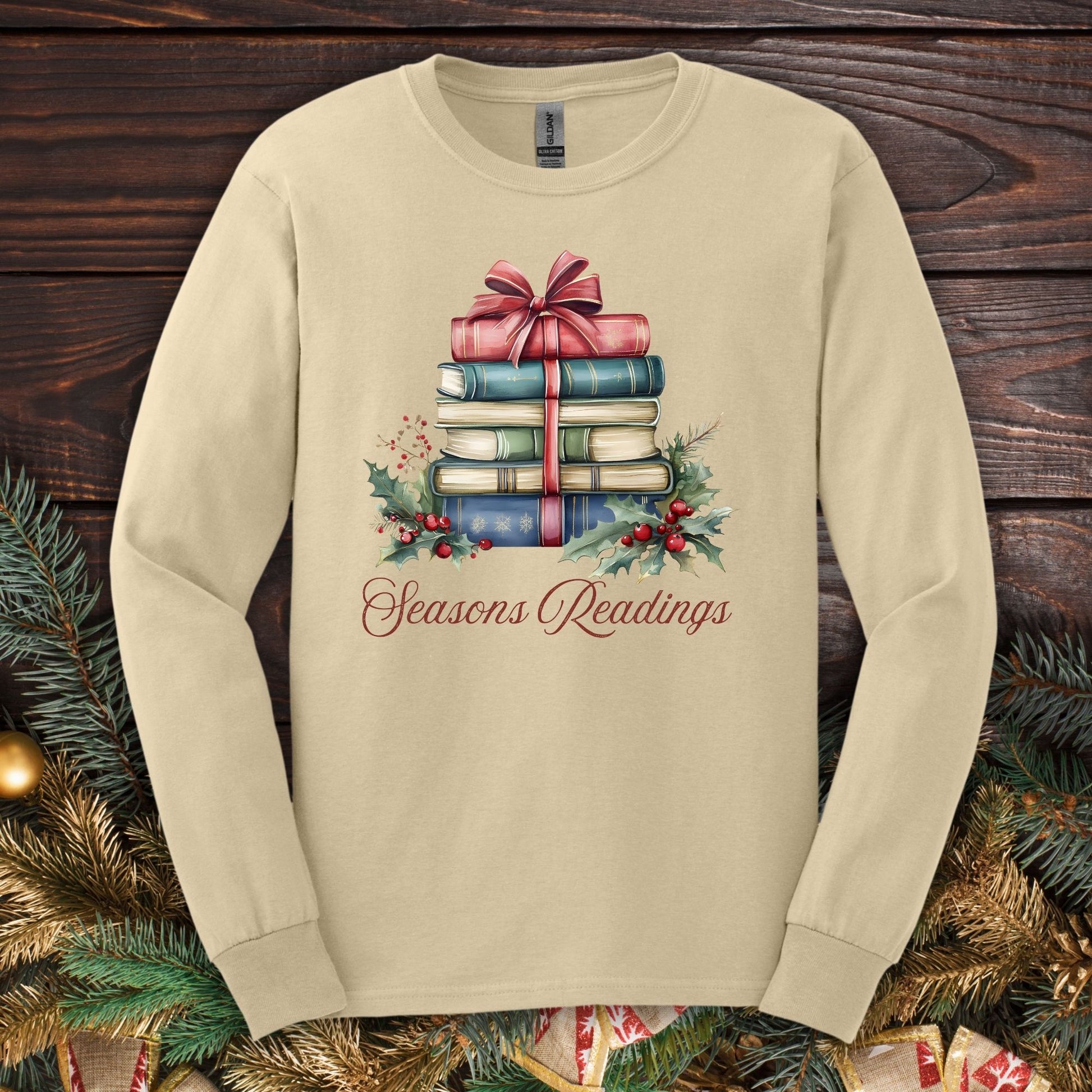 Sand long sleeve tee with watercolor vintage Christmas books, red bow, holly, and "Seasons Readings" text.