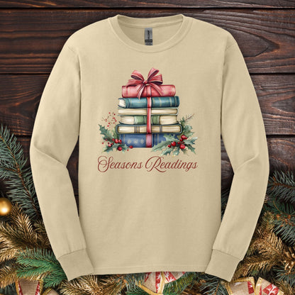 Sand long sleeve tee with watercolor vintage Christmas books, red bow, holly, and "Seasons Readings" text.