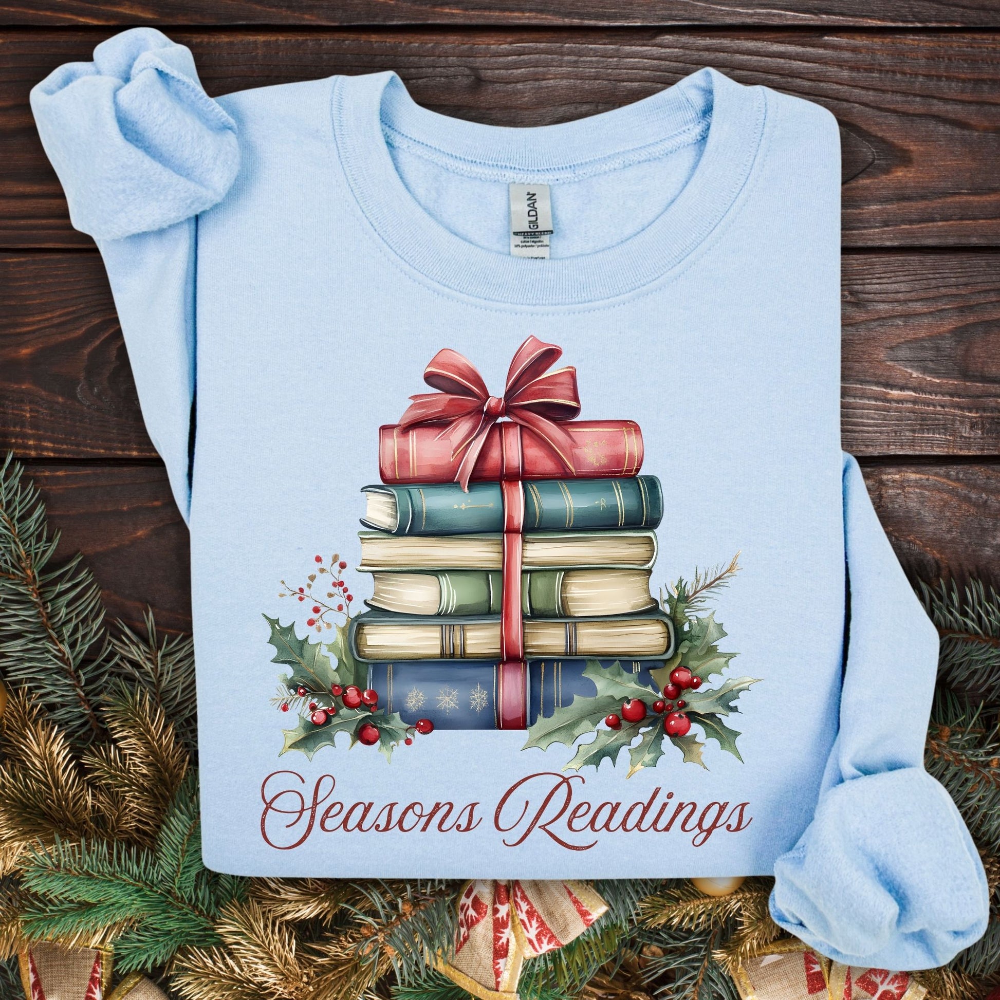 Light blue Seasons Readings sweatshirt with a watercolor stack of vintage Christmas books, holly, and pine.