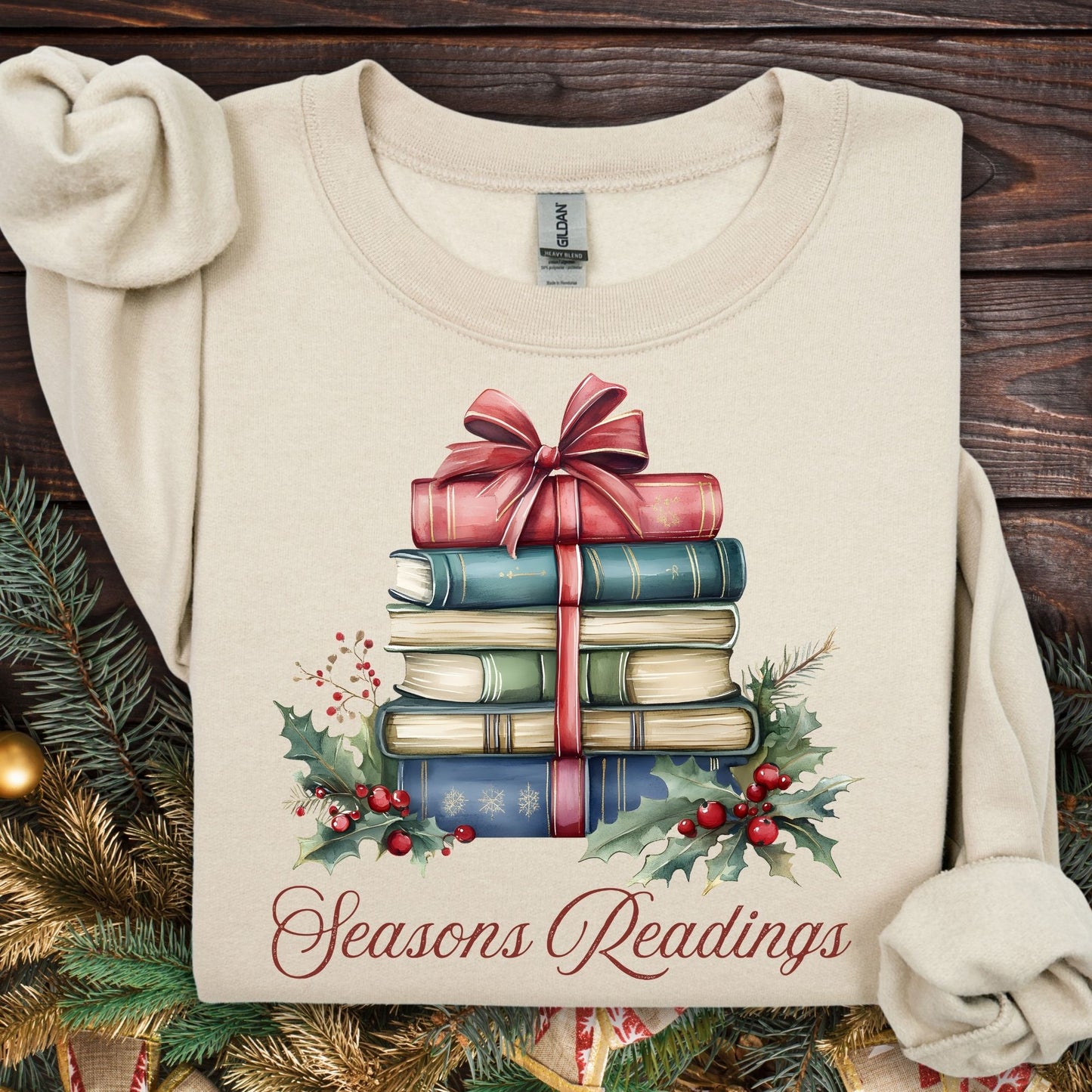 Sand unisex sweatshirt with a watercolor stack of vintage Christmas books, holly, and "Seasons Readings.