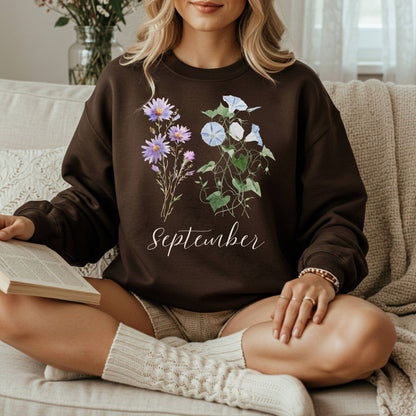 Woman wearing a brown crewneck sweatshirt with watercolor morning glory and aster flowers and "September" text.