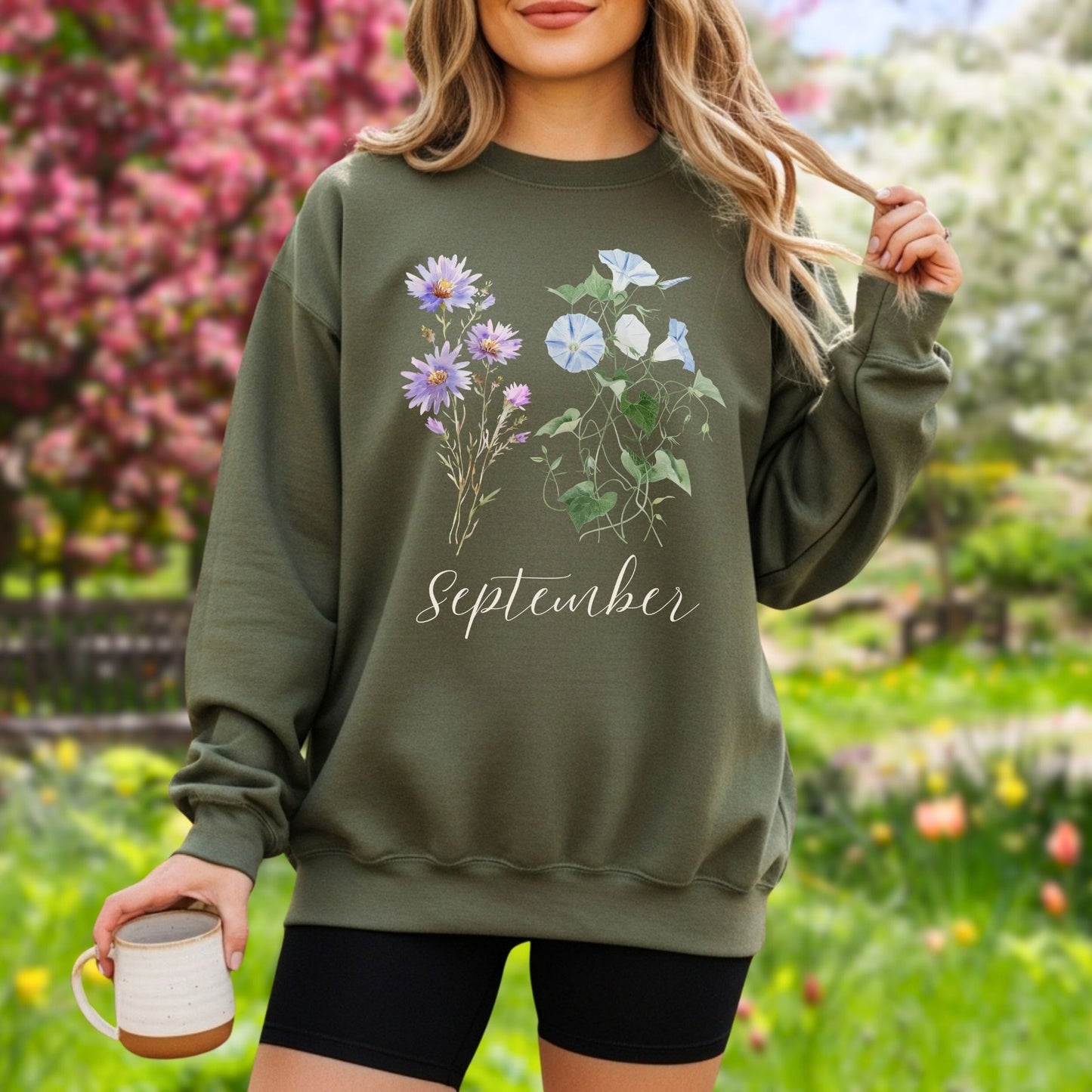 Woman in an olive green crewneck sweatshirt with watercolor morning glory and aster blooms, plus "September" text.