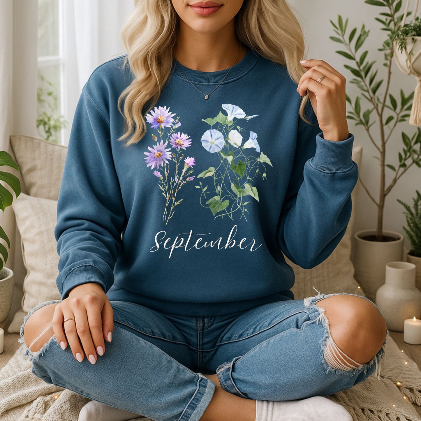 Woman in a blue crewneck sweatshirt with watercolor morning glory and aster flowers and "September" text.