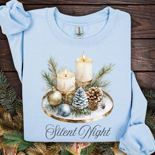 Light blue Gildan sweatshirt with a watercolor "Silent Night" advent arrangement of candles, pinecones, and evergreens.