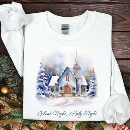 White Gildan fleece sweatshirt with a snowy country chapel design, evergreen garlands, and "Silent Night, Holy Night" text.
