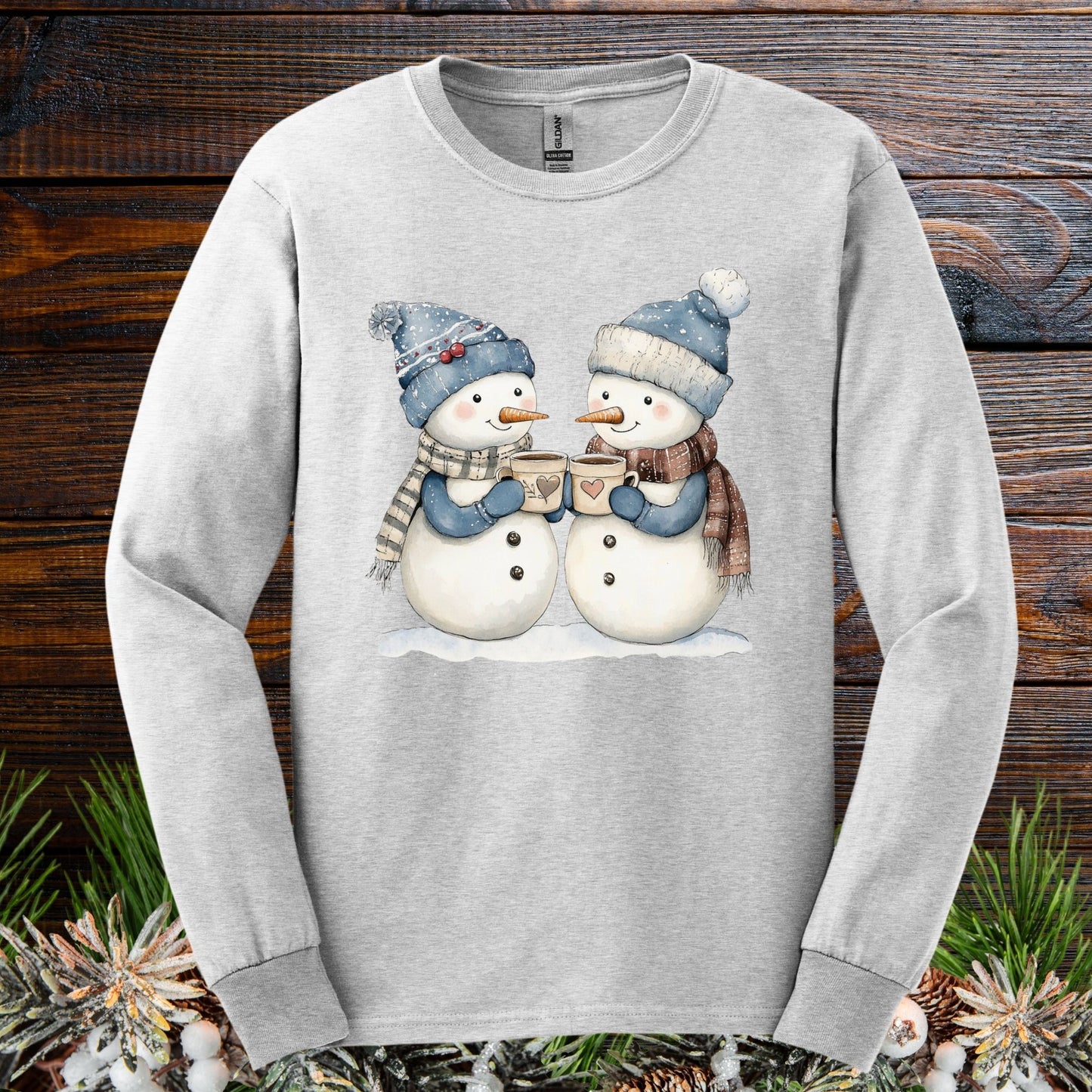Ash long sleeve tee with two snowpeople in blue hats and scarves holding hot chocolate.