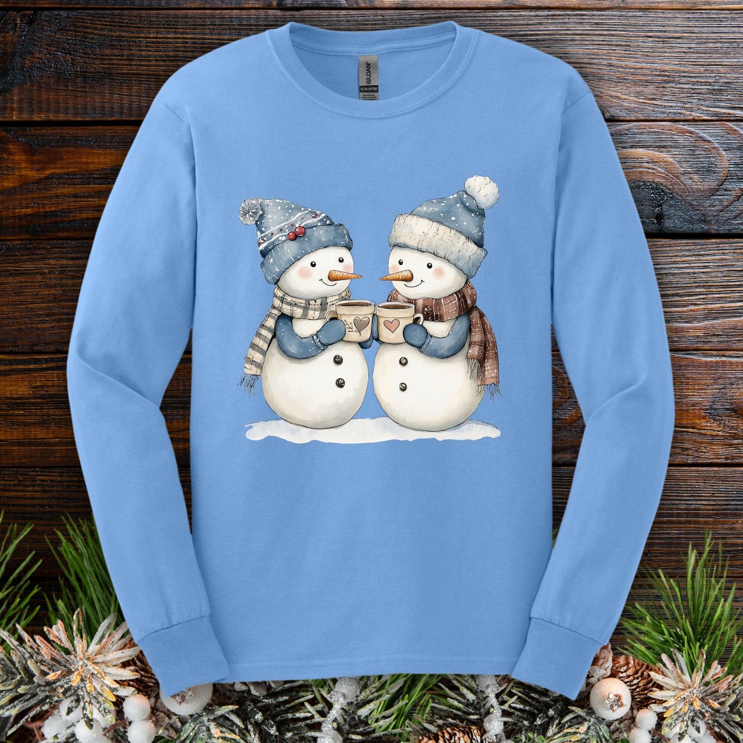 Carolina Blue long sleeve tee with two snowpeople in blue hats, mittens, and scarves holding hot chocolate.