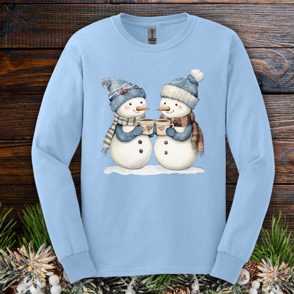 Light blue long sleeve tee with two snowpeople in blue hats, mittens, and scarves holding hot chocolate.