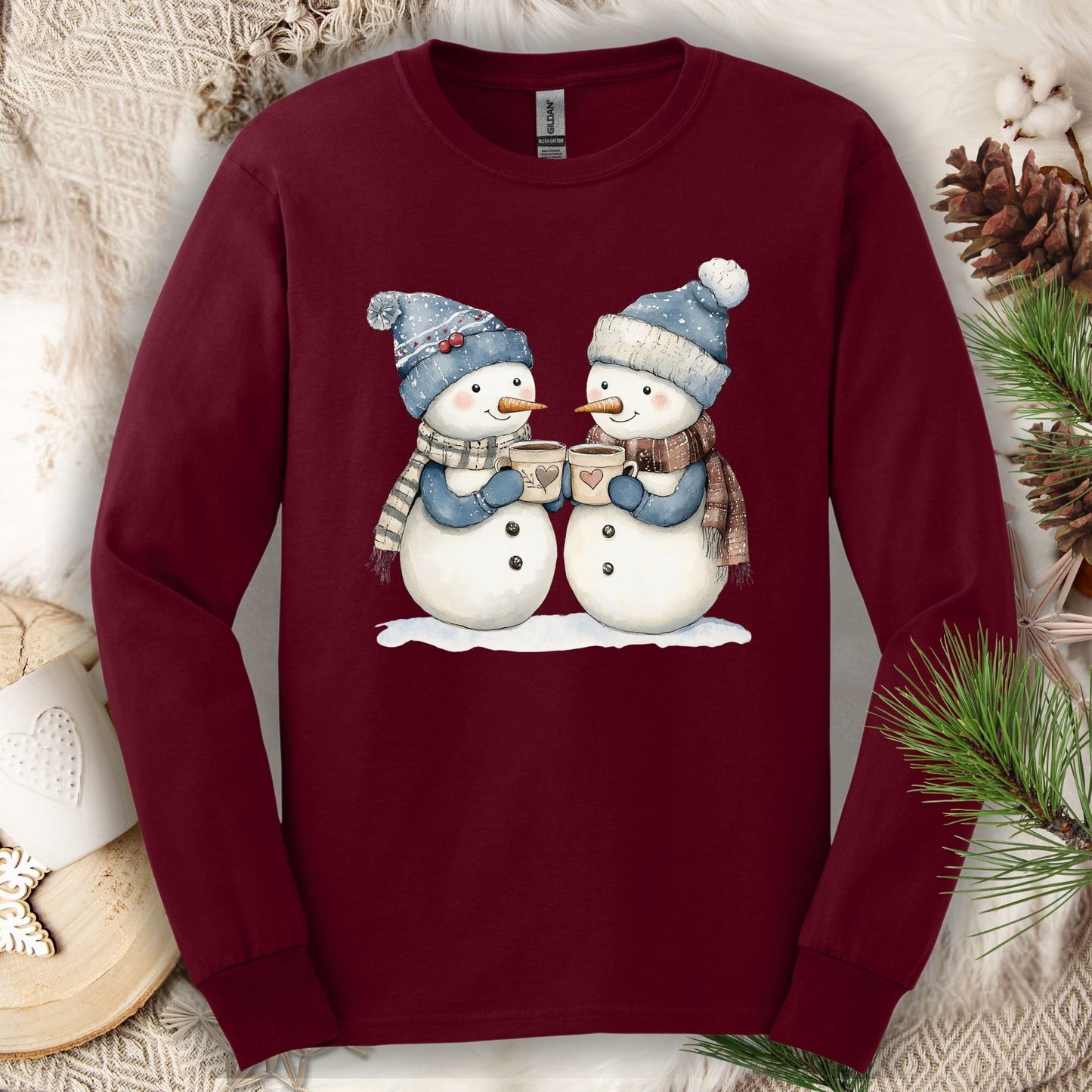 Maroon long sleeve tee with two snowpeople in blue hats, mittens, and scarves drinking hot chocolate.