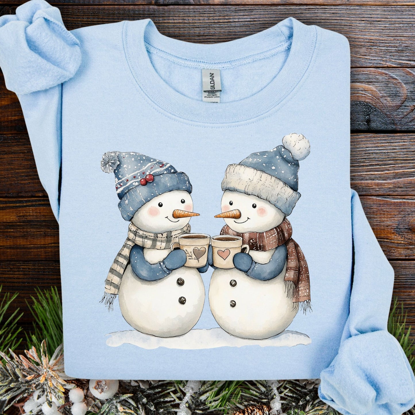 Light blue Snow Couple in Love sweatshirt with two snowpeople in blue hats, holding hot chocolate.