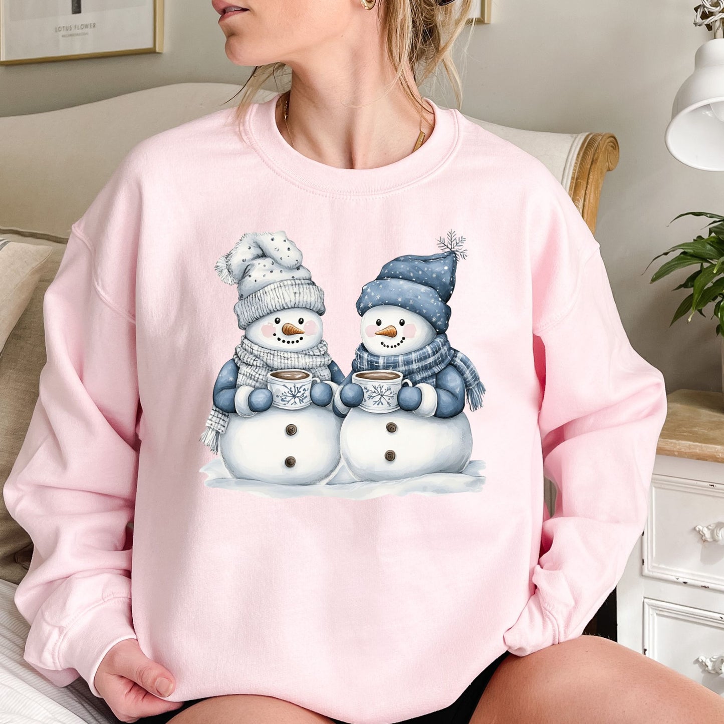 Pink heavy blend sweatshirt with two snowpeople in blue hats and scarves holding hot chocolate.